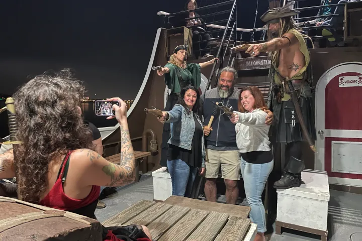 People posing as pirates on a ship with someone taking their picture at night.