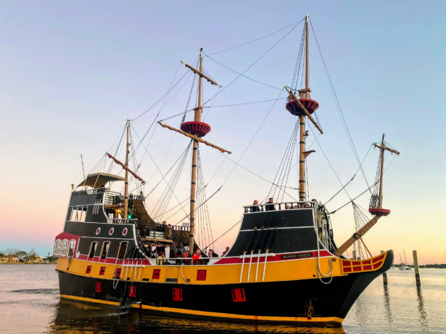 Black pirate ship with red and yellow accents on water at sunset.