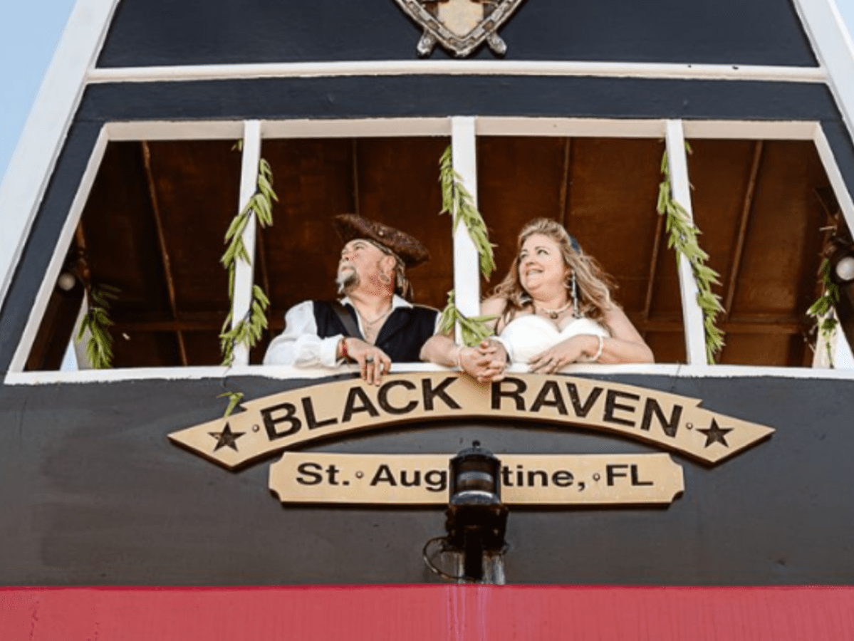 Two people dressed as pirates on a ship balcony labeled 'Black Raven, St. Augustine, FL.'