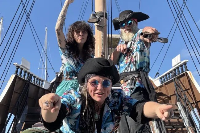Three people dressed as pirates on a ship deck, posing energetically.