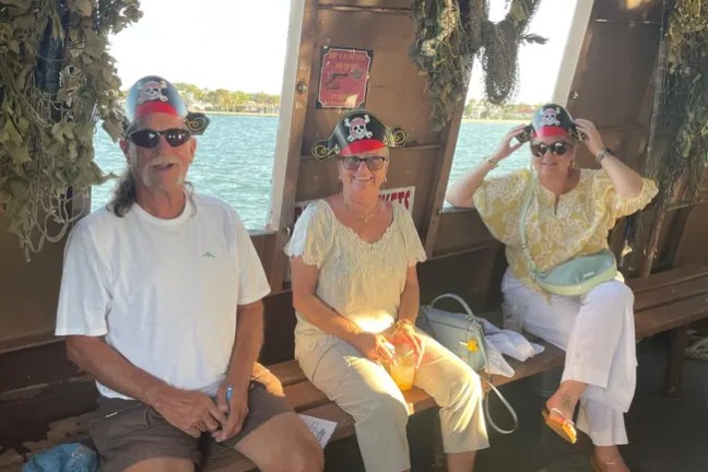 Three people wearing pirate hats on a boat near water.