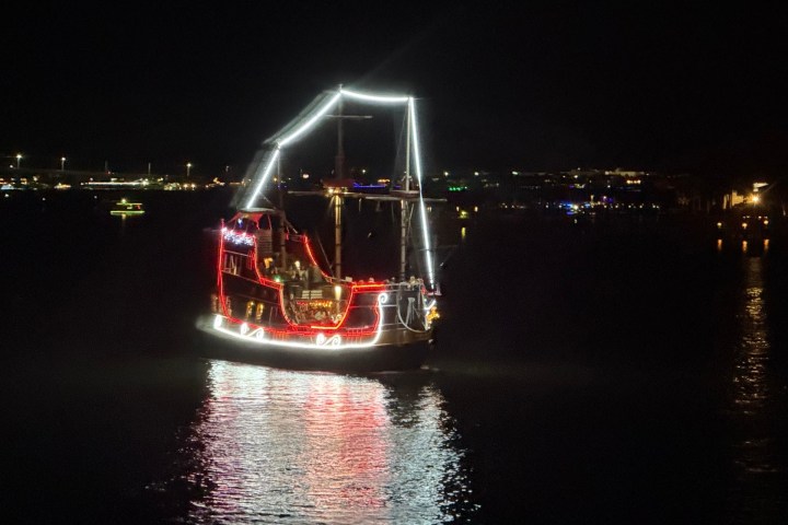 Sailboat with festive lights on a dark night, reflecting on water.