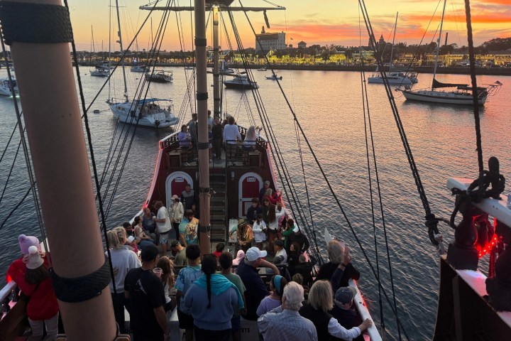 Crowd on a ship's deck at sunset in a marina with other boats.