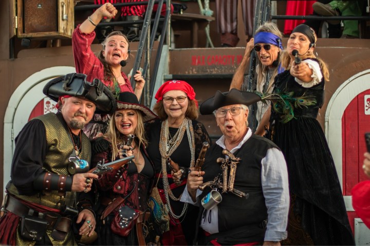 Group of people in pirate costumes, some holding props, posing enthusiastically outdoors.