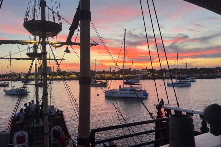 Sailboats on calm water under a colorful sunset sky.