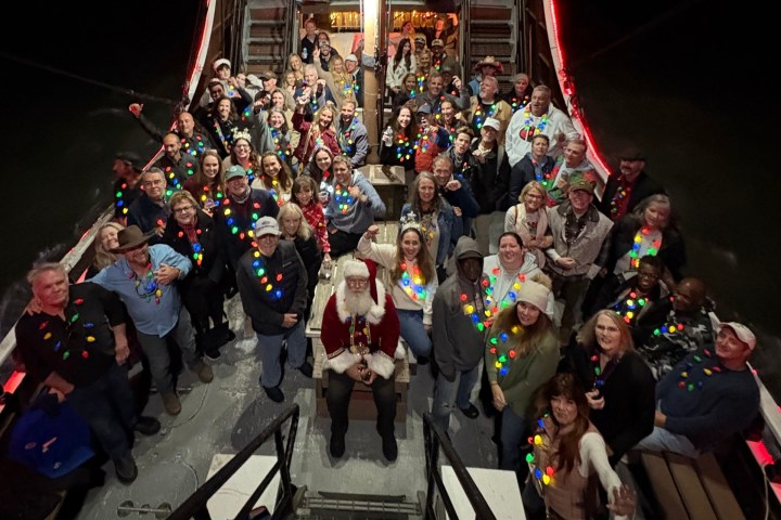 Group photo with people wearing multicolored light necklaces, centered around a person dressed as Santa.
