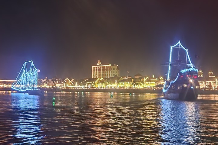 Two boats with blue lights on a reflective water surface at night near a lit cityscape.